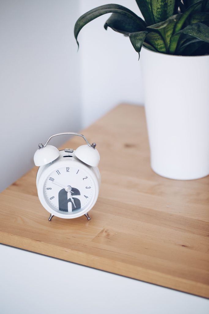 sleep schedule for remote workers white alarm clock on light wood table